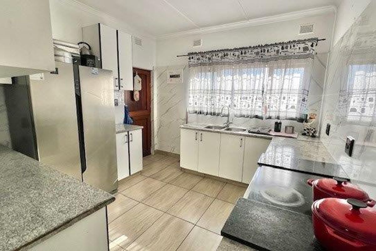 A functional kitchen featuring granite countertops, double basin sink, white cabinetry, and marble-look wall tiles with tiled flooring throughout.