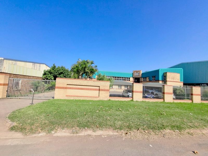 Front exterior view of a commercial property featuring a brick perimeter wall, metal security fencing, and a gated entrance with corrugated metal roofing.