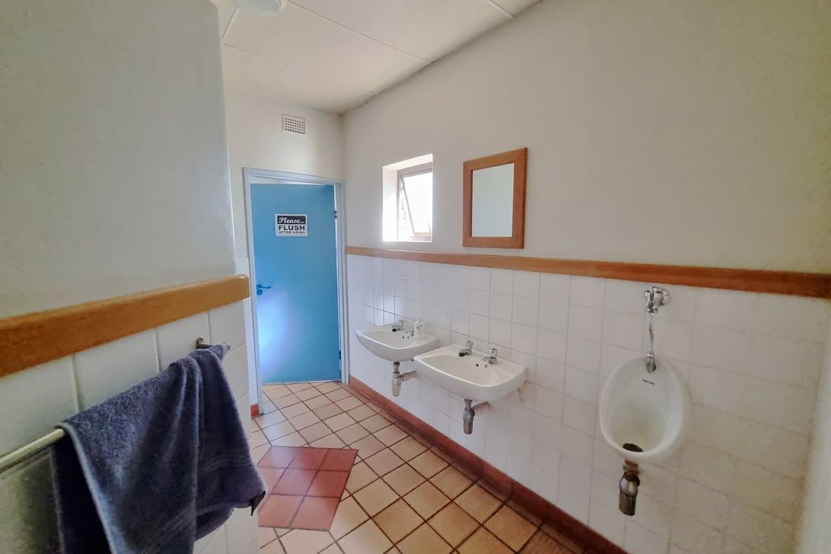 A functional commercial restroom featuring wall-mounted washbasins, a urinal, and tiled surfaces, presenting a dated aesthetic suitable for modernization.