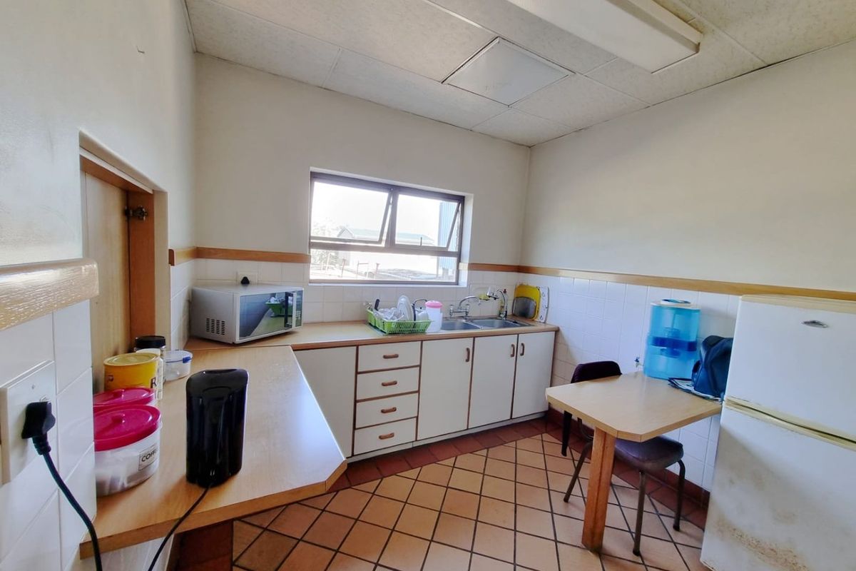 Functional commercial kitchenette featuring built-in cabinetry, laminate countertops, stainless steel sink, and tiled flooring, suitable for office or staff breakroom use.