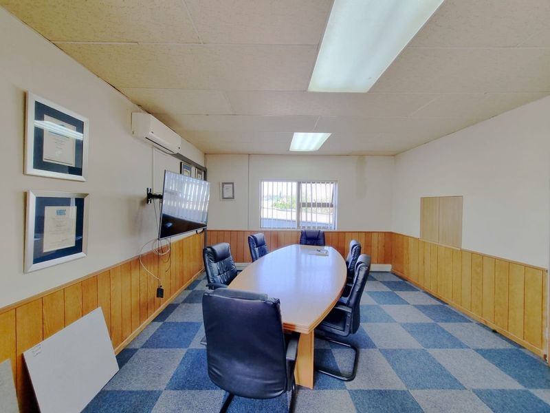 A functional office meeting room featuring wood paneling, carpet tiles, fluorescent lighting, and an installed air conditioning unit.