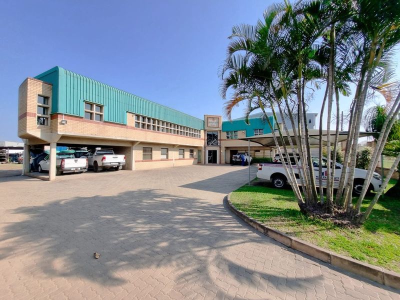 Front exterior view of a commercial property featuring a brick facade, metal roofing, and a spacious paved driveway with covered parking.