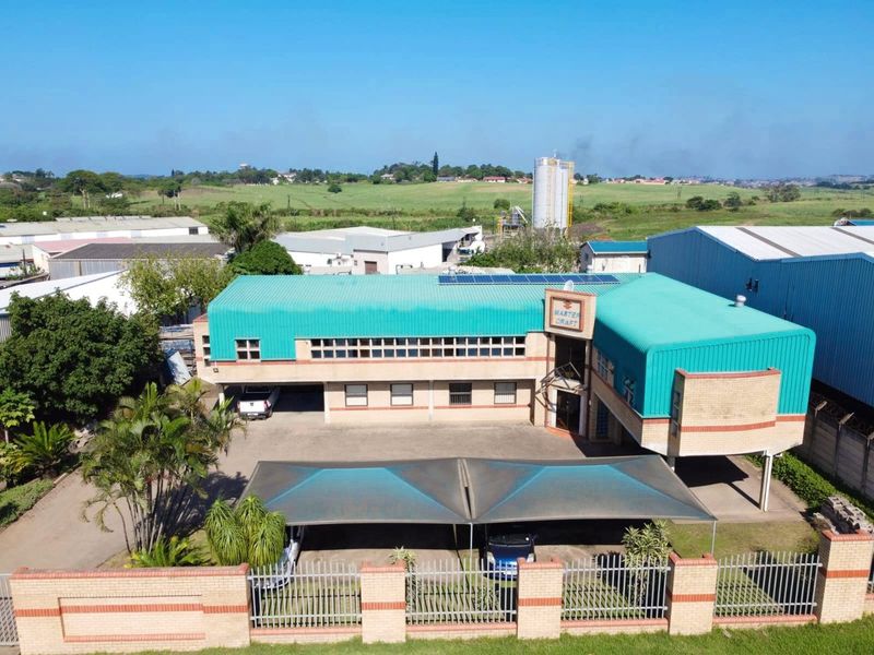 Aerial view of a commercial property featuring a metal roof with solar panels, brick facade, paved driveway, and a shaded parking area.