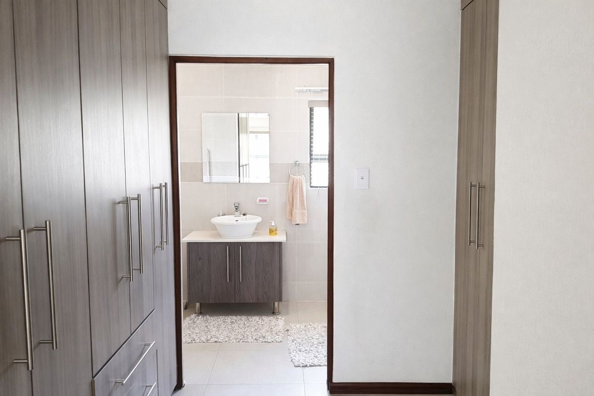 A clean bathroom featuring a modern vessel sink on a vanity cabinet, complemented by built-in cupboards in the adjacent dressing area.