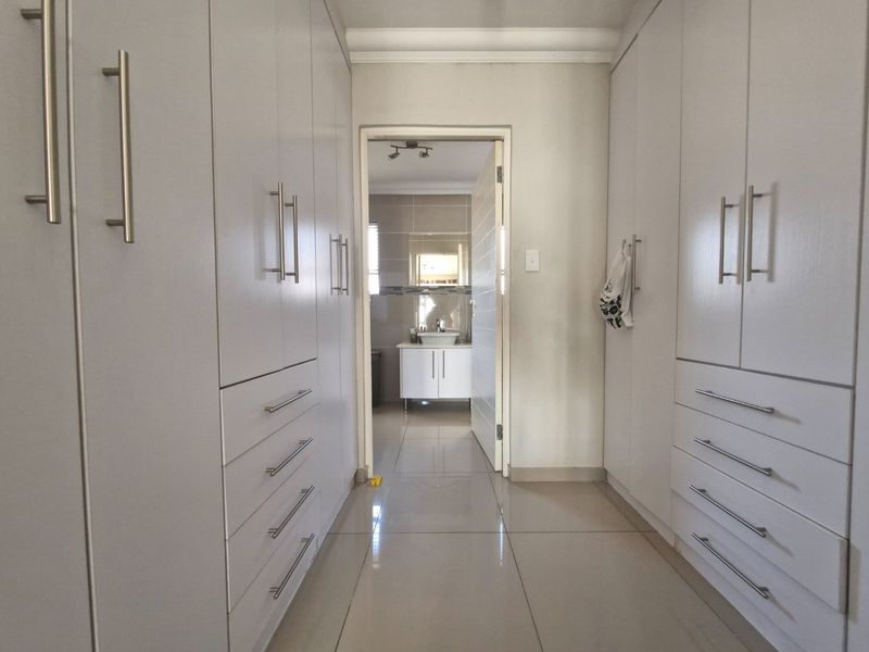 A clean dressing area featuring extensive built-in cupboards with modern handles, tiled flooring, and direct access to an en-suite bathroom.