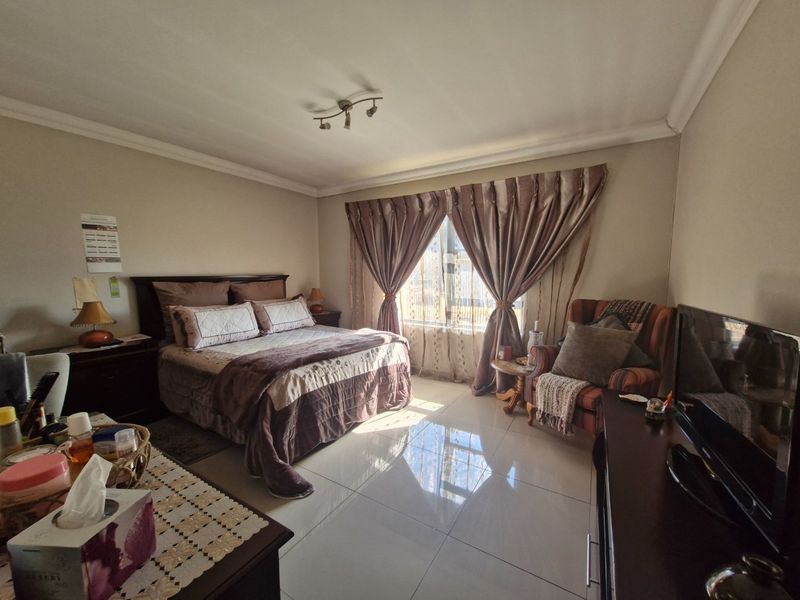 A well-lit bedroom featuring large format floor tiles, neutral wall tones, and a window with curtain treatments.