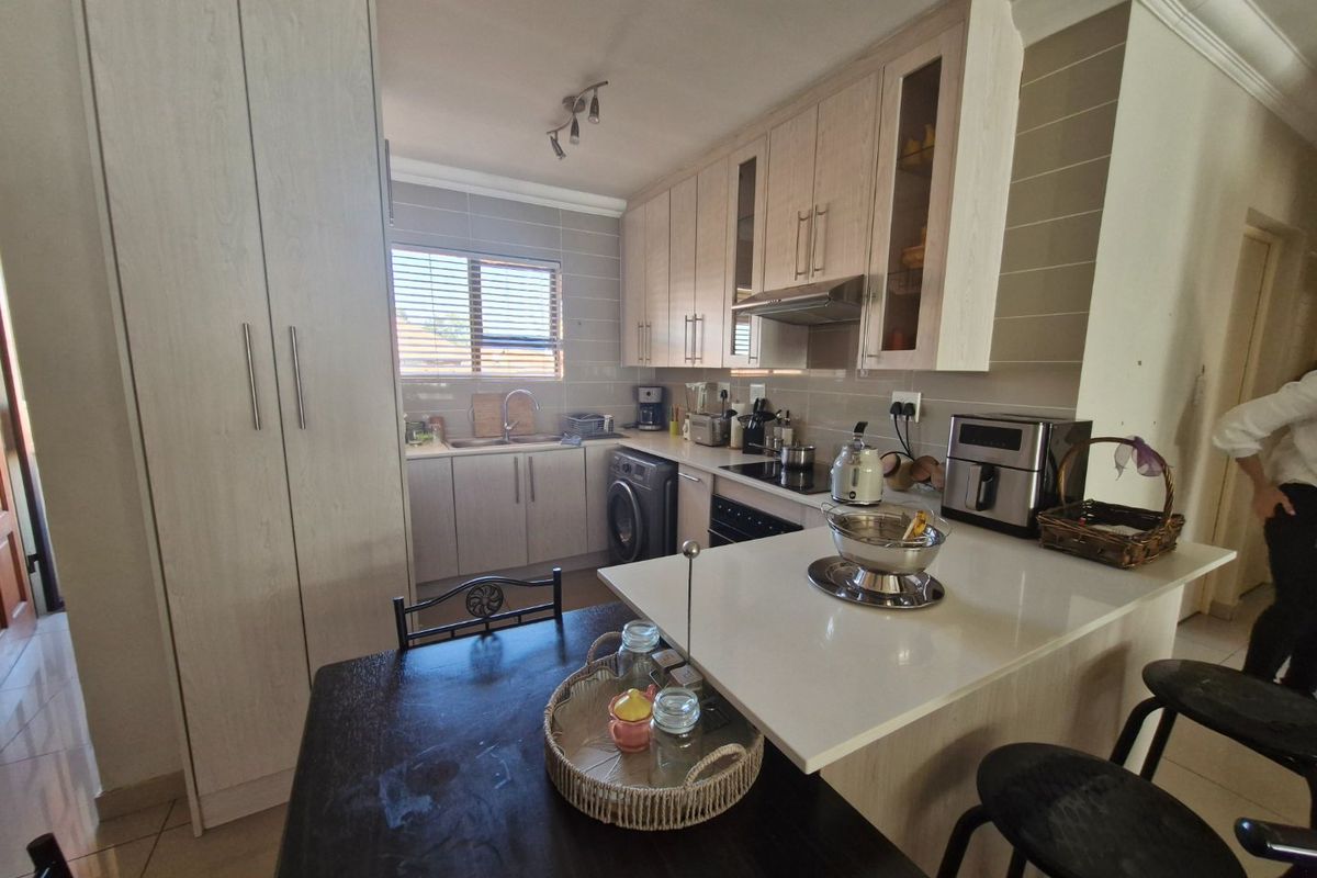 A functional kitchen featuring light wood cabinetry, stone countertops, integrated appliances, and a breakfast bar area with a tiled backsplash.