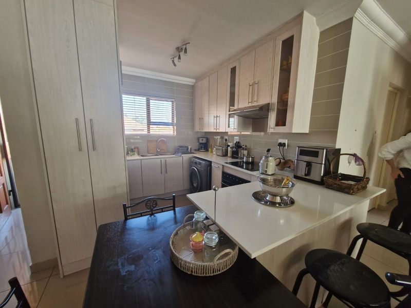 A functional kitchen featuring light wood cabinetry, stone countertops, integrated appliances, and a breakfast bar area with a tiled backsplash.