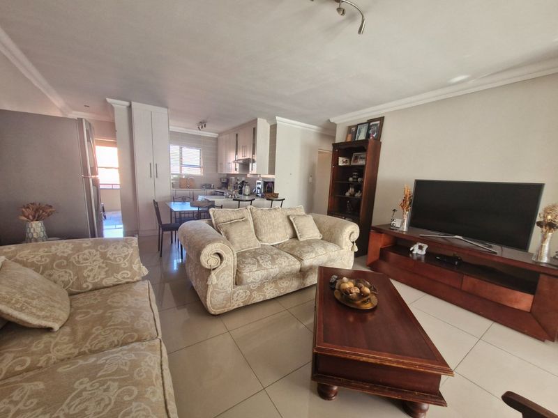An open-plan living and kitchen area featuring tiled flooring, neutral walls, and functional built-in cabinetry, creating a cohesive and practical living space.