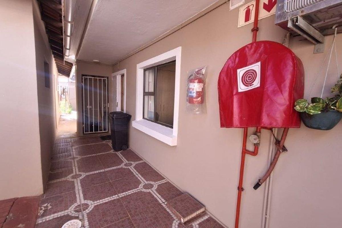A paved exterior side passage featuring a fire hose reel, fire extinguisher, and secure access gate.