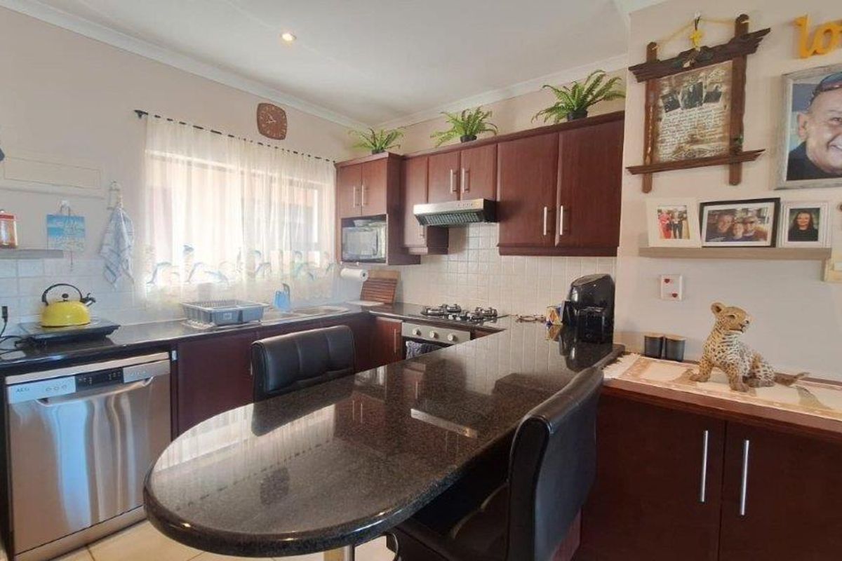 A functional kitchen featuring dark wood cabinetry, granite countertops, a breakfast bar, and built-in appliances including a gas hob and oven.