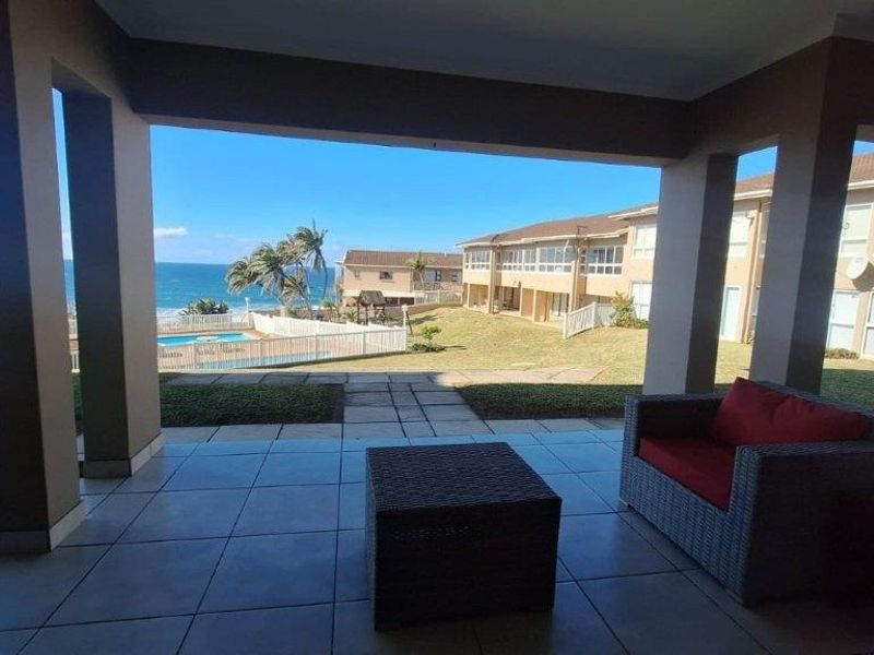 Spacious covered patio featuring tiled flooring and concrete pillars, offering direct access to the garden and scenic ocean views.