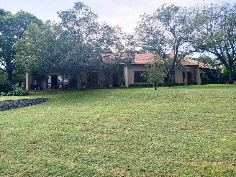 A view of the rear elevation of the farm house, featuring a spacious lawn, stone accents, and a terracotta tiled roof.