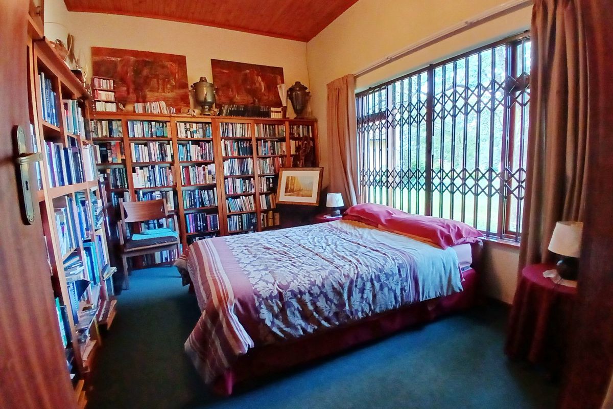 A bedroom featuring built-in wooden bookshelves, a timber-paneled ceiling, and a large window fitted with a security gate.