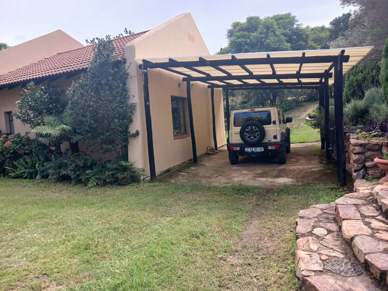 A covered carport structure attached to the side of a farm-style residence, featuring a concrete base and adjacent stone landscaping.