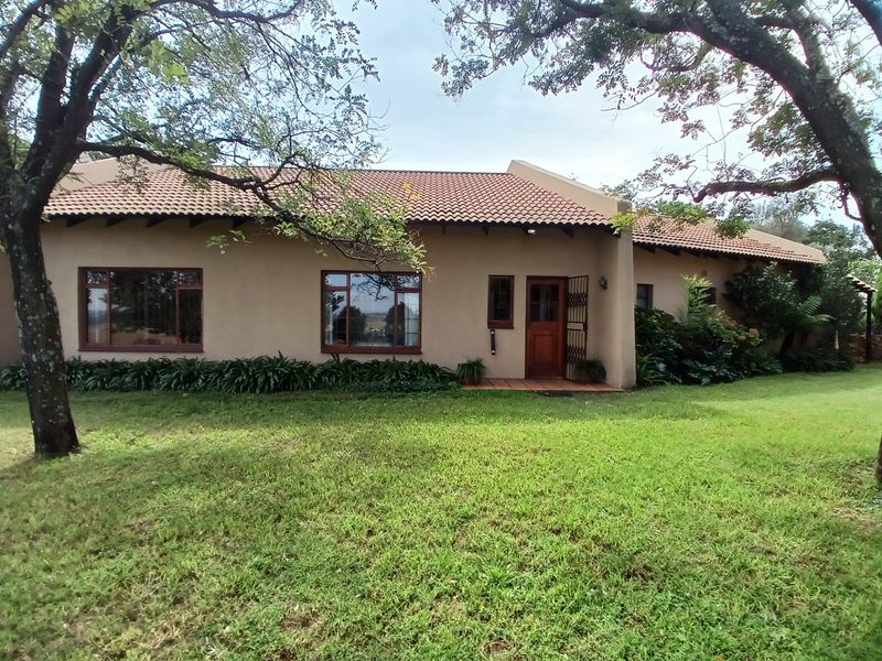Rear view of a farm-style residence featuring terracotta roof tiles, timber-framed windows, and a landscaped garden setting.