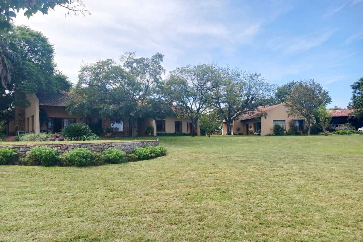 Spacious rear garden featuring a stone retaining wall and well-maintained lawn leading to the main farm dwelling with tiled roofing.