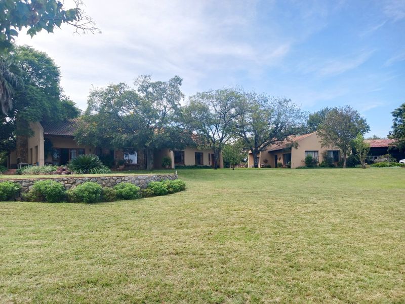 Spacious rear garden featuring a stone retaining wall and well-maintained lawn leading to the main farm dwelling with tiled roofing.