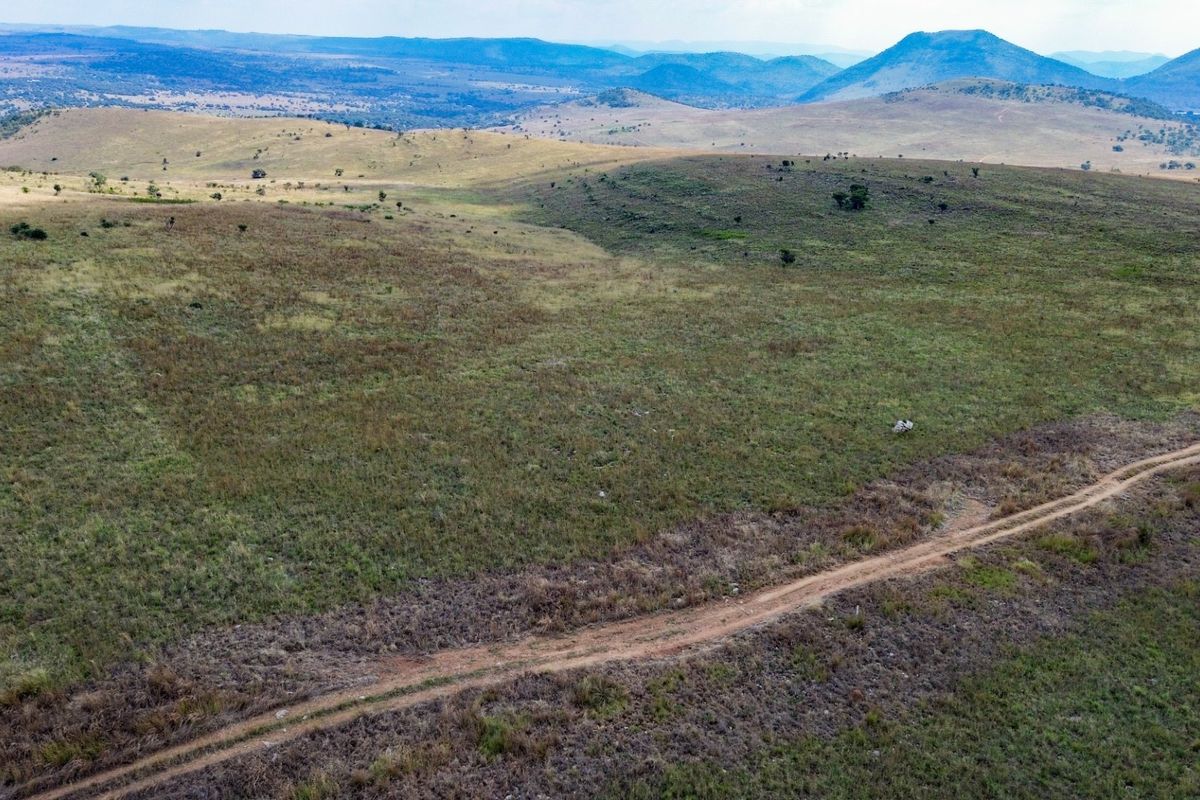 An expansive aerial view of the farm property featuring open grasslands and a dirt access track with distant mountain scenery.