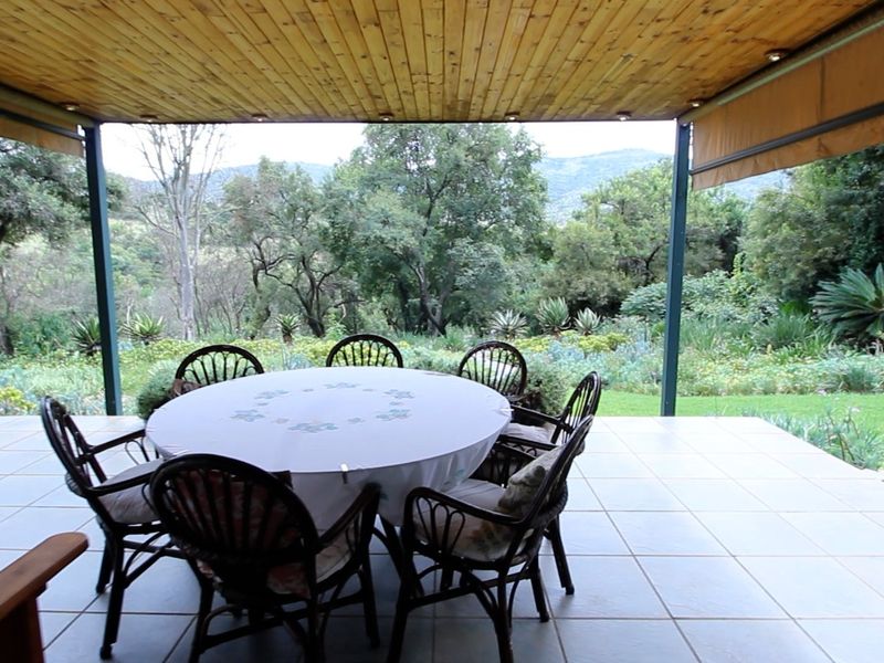 A covered patio featuring a timber-clad ceiling with recessed lighting and tiled flooring, offering expansive views of the surrounding garden and landscape.