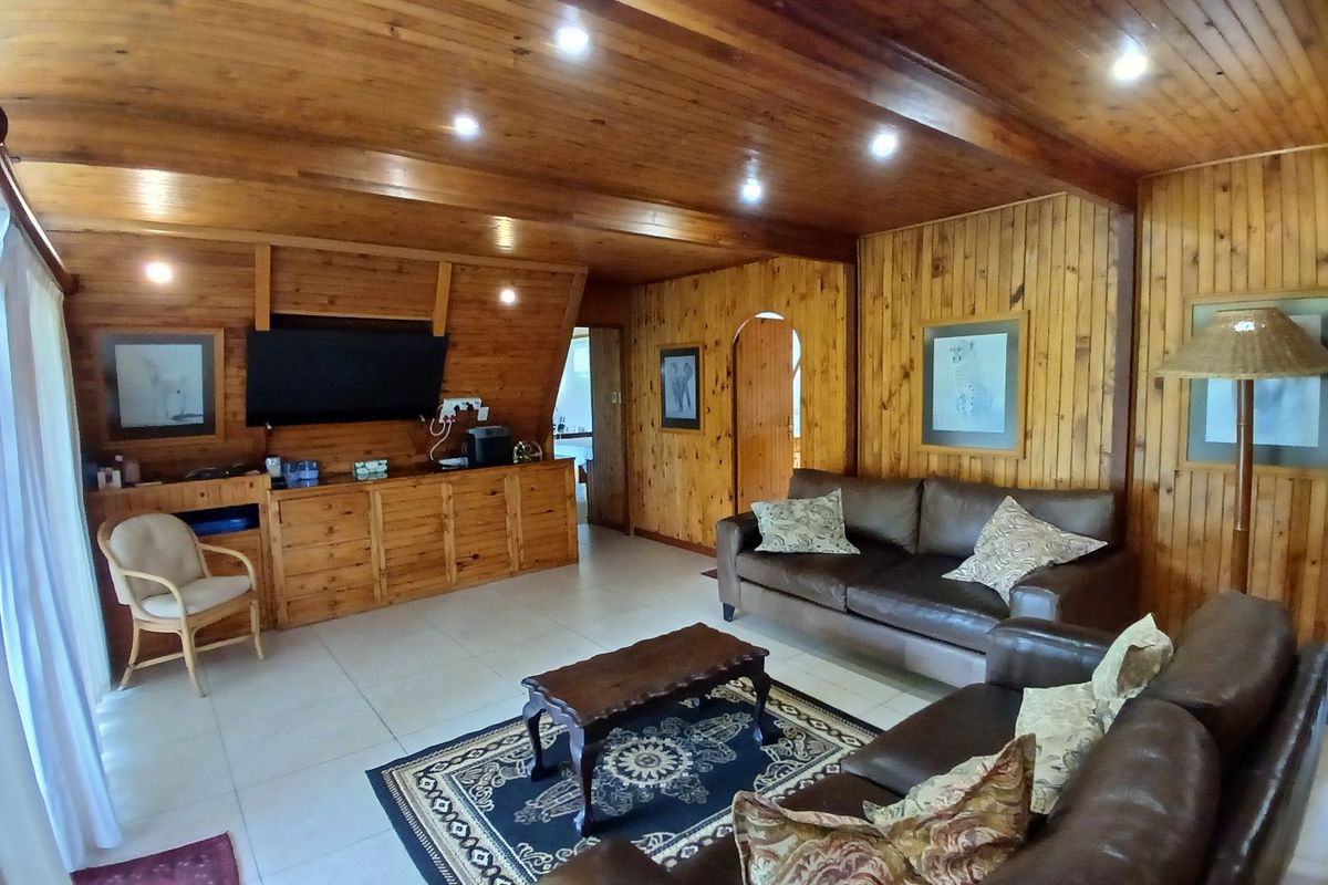 A spacious living room featuring extensive timber wall paneling, a matching timber ceiling with recessed lighting, and neutral tiled flooring.