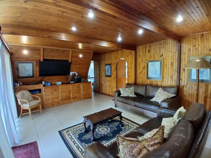 A spacious living room featuring extensive timber wall paneling, a matching timber ceiling with recessed lighting, and neutral tiled flooring.