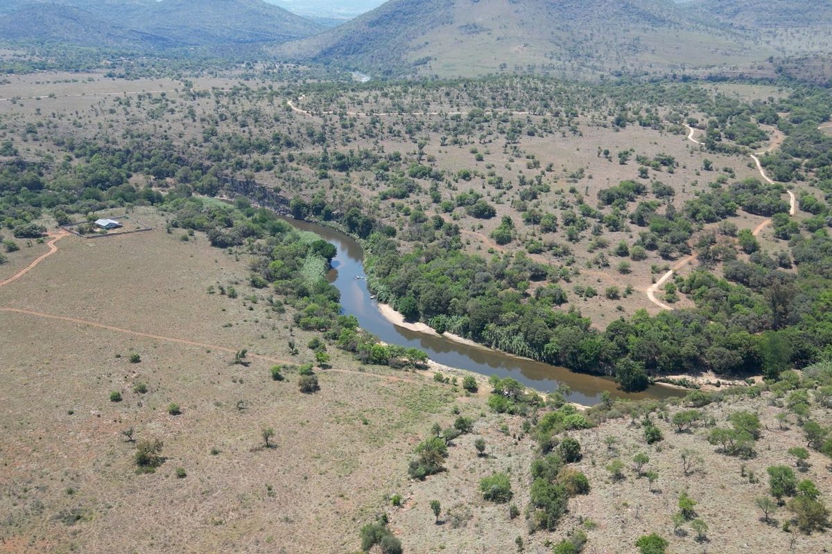 An aerial view of the expansive farm property featuring a winding river, natural bushveld landscape, and established dirt access roads.