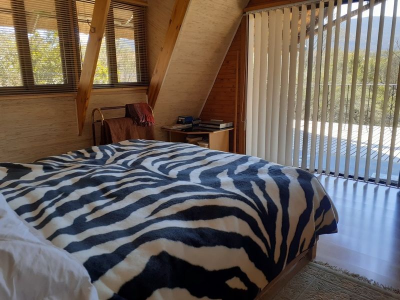 A cozy bedroom featuring exposed timber rafters, wood-paneled walls, and large sliding glass doors that open onto a private balcony with natural light.