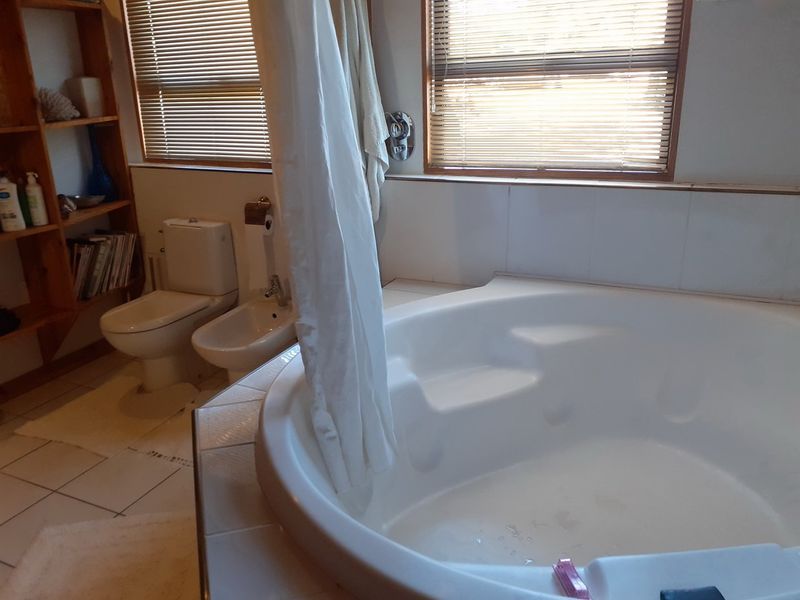 A functional bathroom featuring a built-in corner bathtub, toilet, bidet, and tiled finishes with natural light from dual windows.