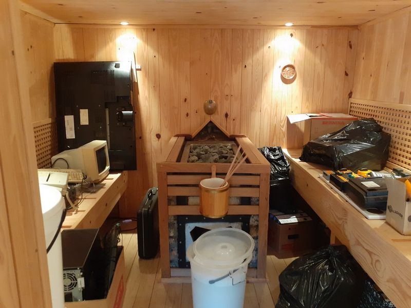 A timber-clad sauna featuring a central heater with rocks and built-in wooden benches, currently utilized for storage.
