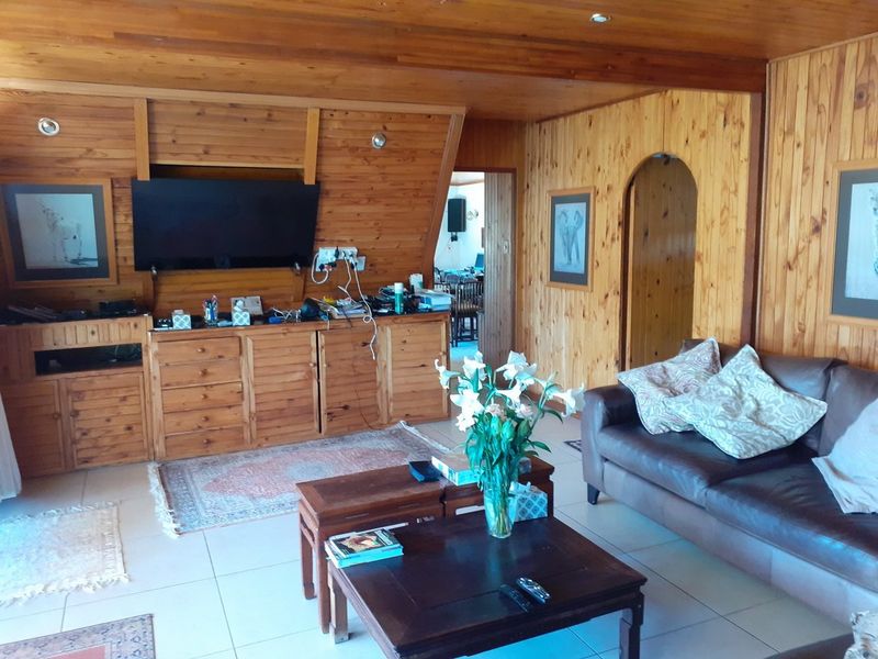 A living room featuring extensive timber wall paneling, a timber ceiling, tiled flooring, and a distinctive arched doorway leading to an adjacent space.