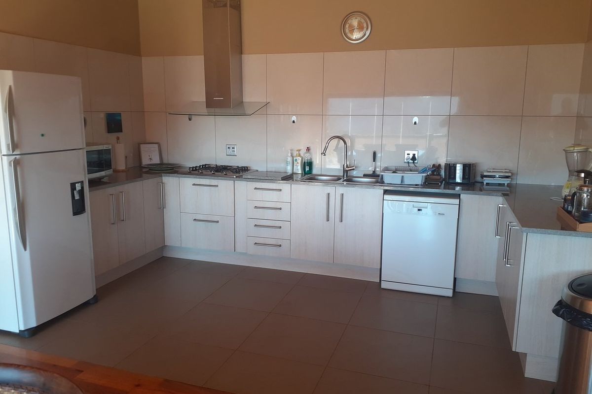 A functional kitchen featuring light-toned cabinetry, a gas hob, stainless steel extractor fan, and tiled splashbacks with neutral floor tiles.