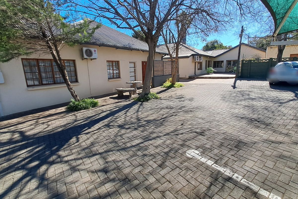 A paved rear courtyard area featuring established trees, split-system air conditioning units, and access to the main building structure.