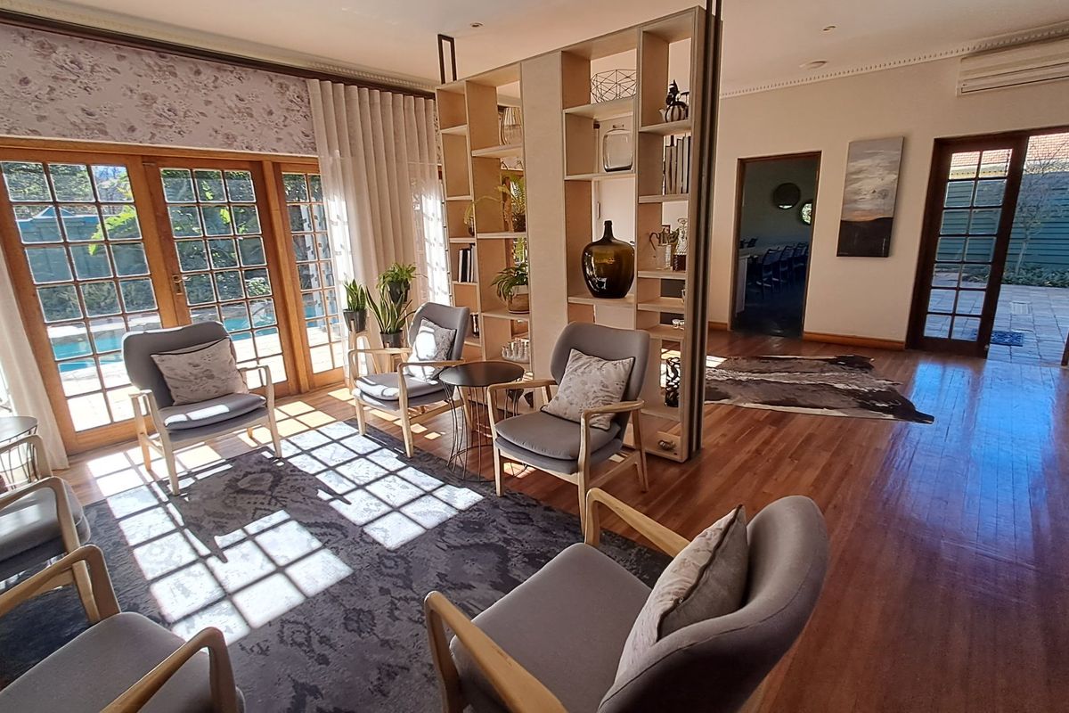 Spacious living area featuring polished hardwood floors, elegant crown molding, and large french doors providing natural light and access to the outdoor pool area.