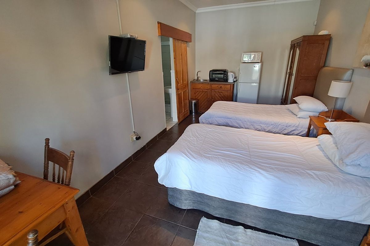 A bedroom featuring tiled flooring, a small kitchenette area with cabinetry and sink, and access to an en-suite bathroom.