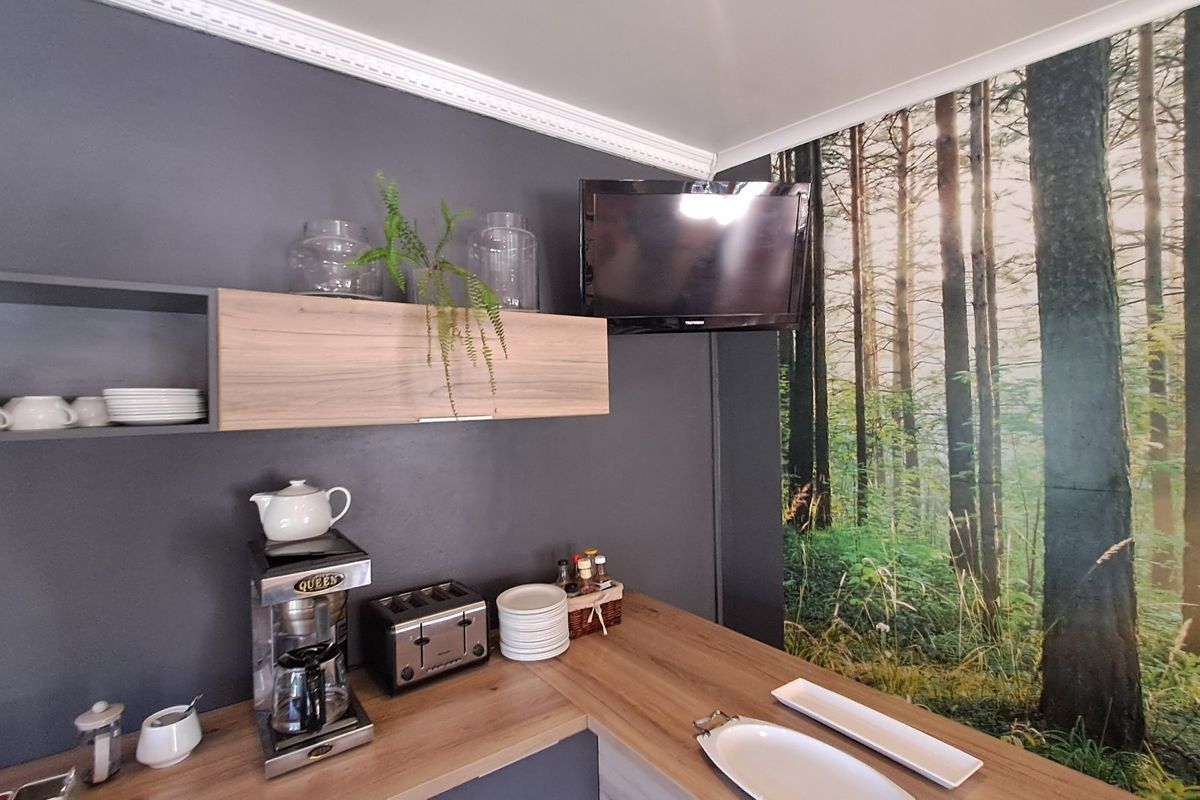A compact kitchen area featuring modern wood-look laminate countertops, wall-mounted cabinetry, and decorative crown molding with a forest-themed feature wall.