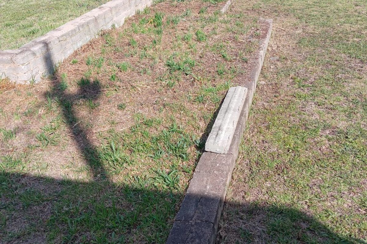 A vacant residential plot featuring established lawn, concrete retaining wall structures, and a perimeter hedge boundary.