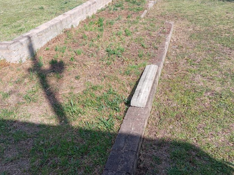A vacant residential plot featuring established lawn, concrete retaining wall structures, and a perimeter hedge boundary.