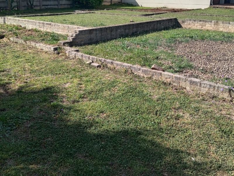 A residential garden area featuring tiered lawn sections, a boundary wall, and a low brick retaining wall structure.