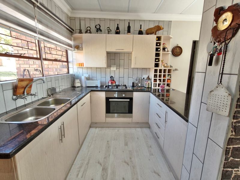 A functional kitchen featuring light wood cabinetry, granite countertops, a built-in oven with gas hob, and a double basin sink with tiled backsplash.