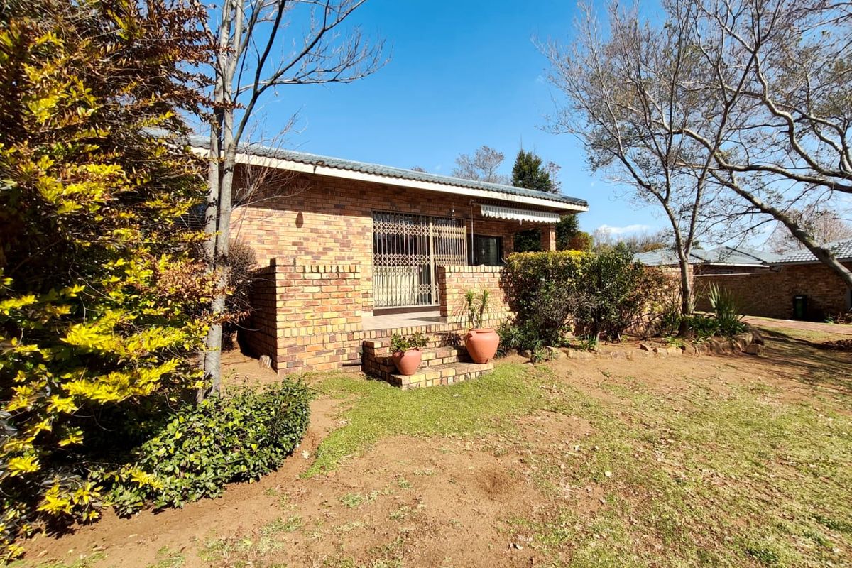 A view of the rear face brick facade of the house, featuring a small patio area with security gate access and surrounding garden space.