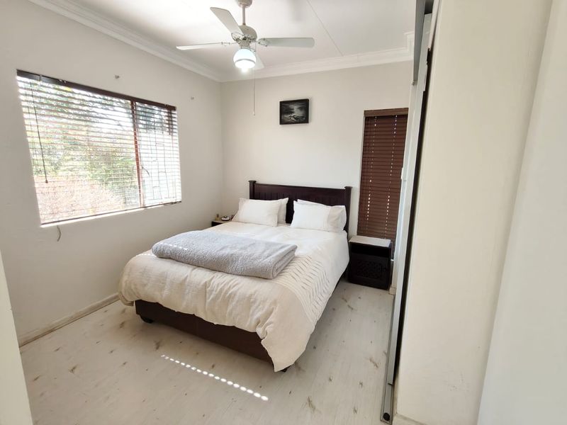 A well-lit bedroom featuring light-toned flooring, built-in cupboards, and a ceiling fan, offering a clean and functional living space.