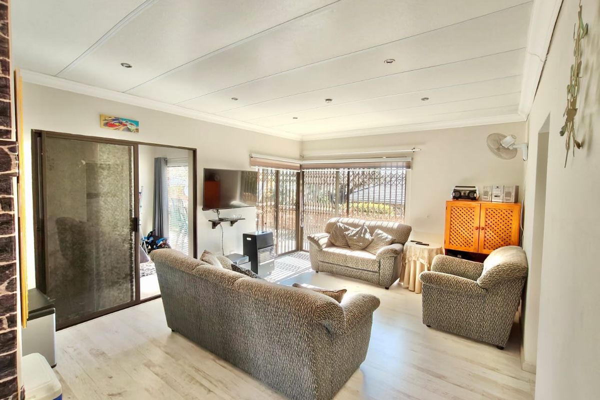 A bright living room featuring light-toned laminate flooring, recessed ceiling lights, and large sliding glass doors with security gates leading to the exterior.