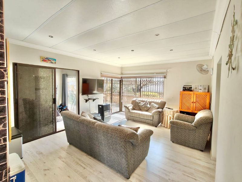 A bright living room featuring light-toned laminate flooring, recessed ceiling lights, and large sliding glass doors with security gates leading to the exterior.