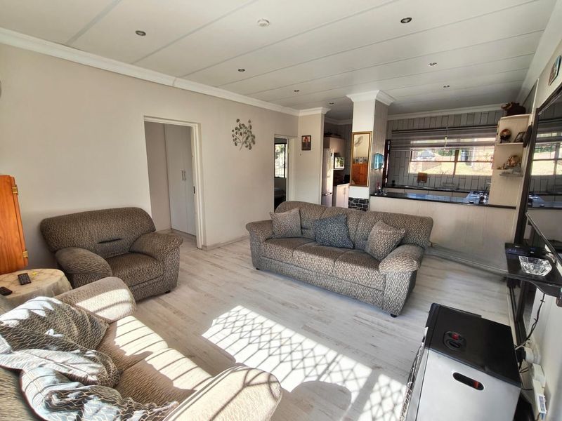 Open-plan living area featuring light laminate flooring, recessed lighting, and a functional kitchen with a breakfast bar and tiled backsplash.