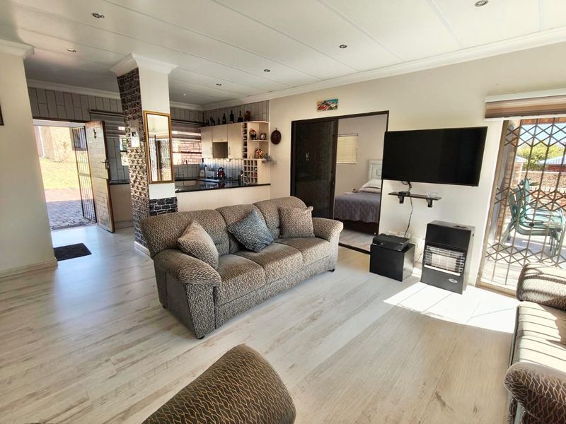 Open-plan living area featuring light laminate flooring, a stone feature pillar, and an integrated kitchen with dark countertops, leading to outdoor access.