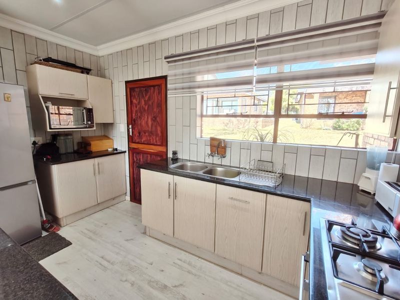 A functional kitchen featuring light wood-finish cabinetry, dark countertops, a gas hob, and a double bowl sink with a window view.