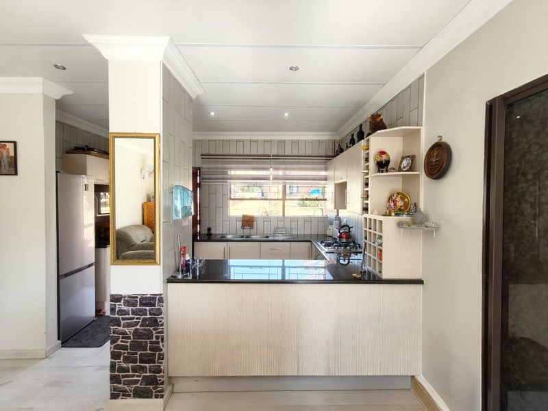 A well-maintained kitchen featuring light wood cabinetry, dark granite countertops, a breakfast bar, and a modern tiled backsplash with integrated gas hob.
