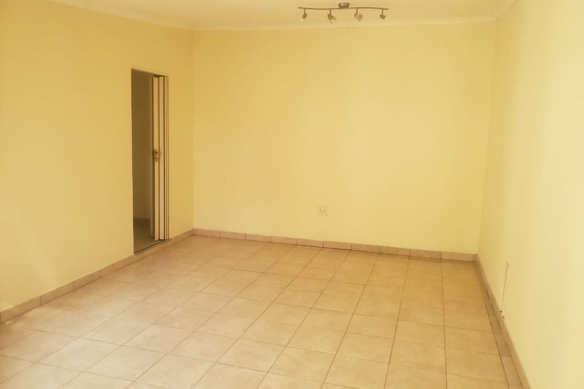 An empty living room featuring neutral tiled flooring, pale yellow walls, and a ceiling-mounted spotlight fixture.