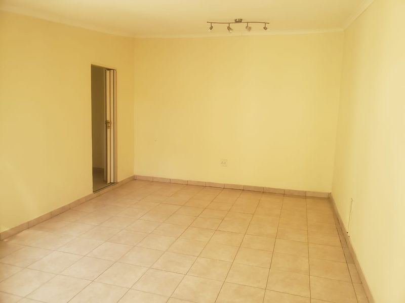 An empty living room featuring neutral tiled flooring, pale yellow walls, and a ceiling-mounted spotlight fixture.